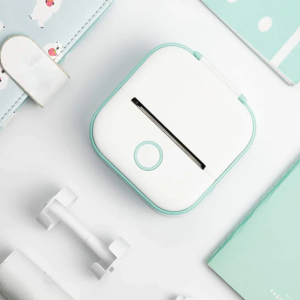 Small white and green electronic device on a light blue surface with stationery items.