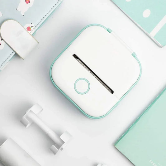 Small white and green electronic device on a light blue surface with stationery items.